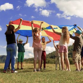 Bambini in cerchio nella natura sorreggono un telo arcobaleno