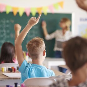 Bimbi in classe alzano la mano davanti alla maestra alla lavagna